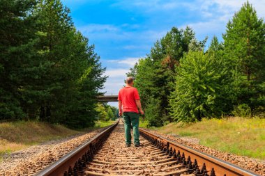 Yalnız adam tren yolunda yürüyor.