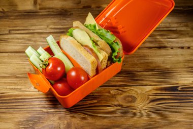 Tahta bir masada sandviç ve taze sebzelerle beslenme çantası.