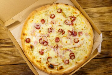 Tahta bir masanın üzerindeki karton kutuda nefis taze pizza. Üst Manzara. Yemek teslimatı, fast food, pizza teslimatı.