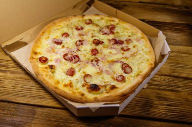 Tahta bir masanın üzerindeki karton kutuda nefis taze pizza. Yemek teslimatı, fast food, pizza teslimatı.