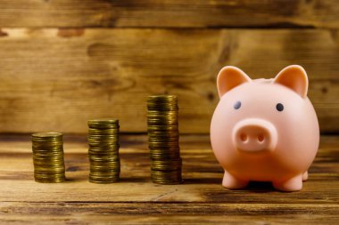 Pembe domuz kumbarası ve tahta arka planda yığınla bozuk para. Para biriktirme kavramı