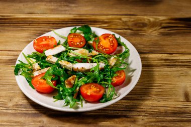 Lezzetli tavuk göğsü salatası, taze roka ve ahşap masada kiraz domatesleri.
