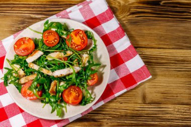 Lezzetli kızarmış tavuk göğsü salatası, taze roka ve ahşap masada kiraz domatesleri. Üst görünüm