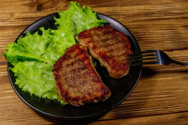 Ahşap masada marul yapraklı ızgara domuz bifteği.