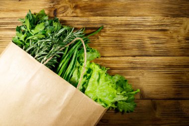 Yeşil soğanlı kağıt torbası, biberiye, marul yaprakları ve ahşap masada maydanoz. Üst Manzara. Sağlıklı gıda ve market alışverişi kavramı