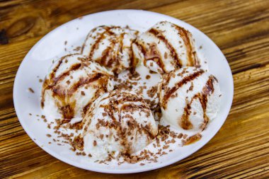 Tahta bir masada beyaz tabakta çikolatalı vanilyalı dondurma.