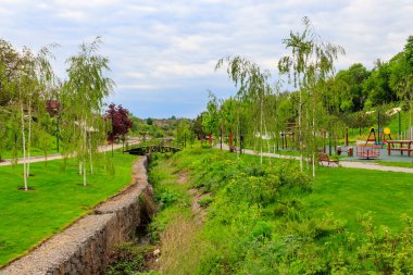 Şehir parkının güzel manzarası küçük nehir ve genç ağaçlar arasında kemerli yaya köprüsü var.