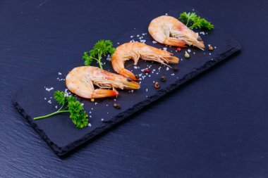 Siyah arkaplanda maydanozlu, tuzlu ve biberli büyük çiğ karidesler.