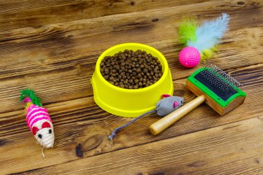 Kasede kuru kedi maması, kedi oyuncakları ve ahşap arka planda evcil hayvan fırçası. Hayvan bakımı konsepti