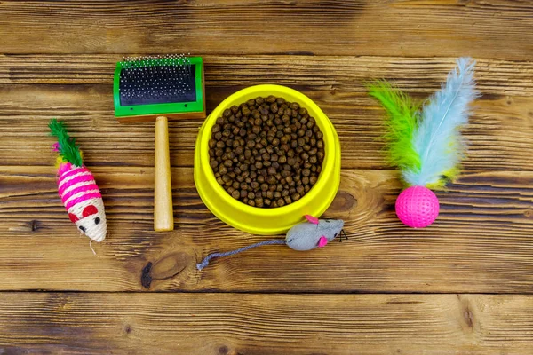Kasede kuru kedi maması, kedi oyuncakları ve ahşap arka planda evcil hayvan fırçası. Üst Manzara. Hayvan bakımı konsepti