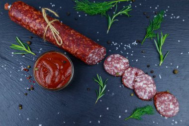 Ketçaplı salam sosisi ve siyah tahtada baharatlar. Üst görünüm