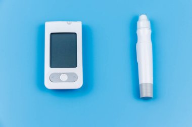 Pastel mavi arka planda dijital glukometre ve tükenmez kalem. Üst Manzara. Diyabet kavramı