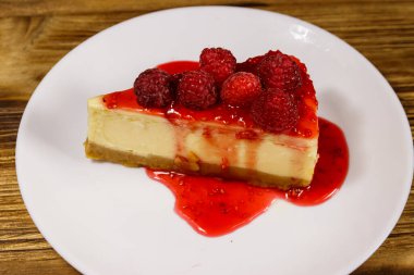 Ahududu ve ahududu reçelli lezzetli New York peynirli keki ahşap masada beyaz bir tabakta.