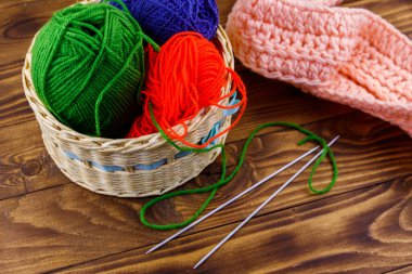 Hasır sepet, renkli örgü iplikleri, örgü iğneleri ve ahşap masa üzerine örülmüş eşarp.