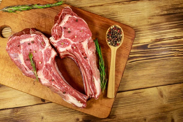 Kemiğin üzerinde çiğ biftek, baharatlar ve ahşap masada biberiye. Üst görünüm