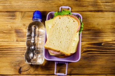 Sandviç ve ahşap bir masada bir şişe su ile beslenme çantası. Üst görünüm
