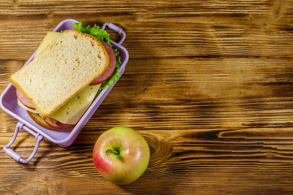 Tahta bir masanın üzerinde sandviç ve elma olan beslenme çantası. Üst görünüm, alanı kopyala