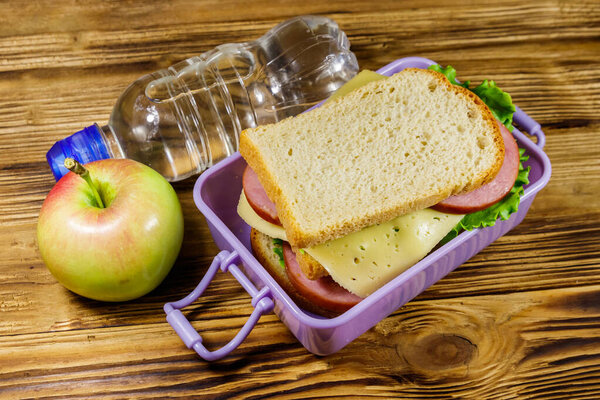Коробка с бутербродами, бутылка воды и яблоко на деревянном столе