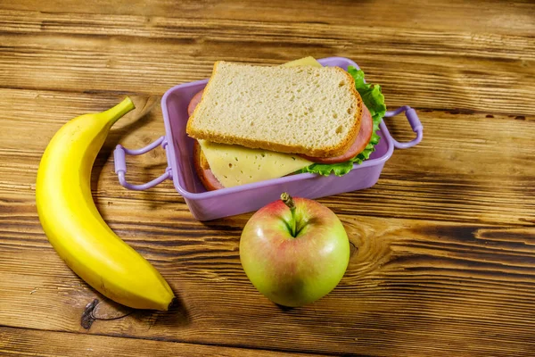 Sandviç, muz ve elmayla birlikte ahşap bir masada.