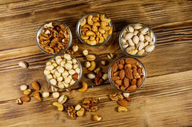 Ahşap masada fındık çeşitleri. Badem, fındık, şam fıstığı, ceviz ve cam kaselerde ceviz. Üst Manzara. Sağlıklı yeme kavramı