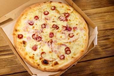 Tahta bir masanın üzerindeki karton kutuda nefis taze pizza. Üst Manzara. Yemek teslimatı, fast food, pizza teslimatı.