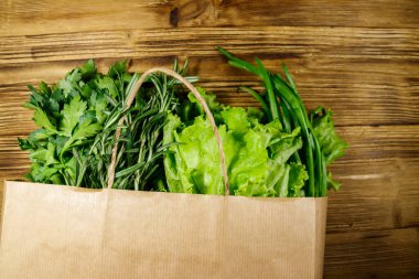 Yeşil soğanlı kağıt torbası, biberiye, marul yaprakları ve ahşap masada maydanoz. Üst Manzara. Sağlıklı gıda ve market alışverişi kavramı