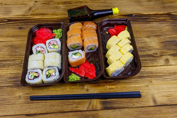 Set of sushi rolls in plastic boxes, soy sauce and chopsticks on wooden table. Sushi for take away or delivery of sushi in plastic containers