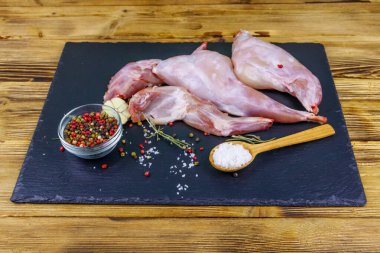 Çiğ tavşan bacağı ve siyah tahta tahta üzerinde baharatlar.