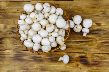 Tahta masada hasır sepetin içinde taze şampiyon mantarları. Üst görünüm