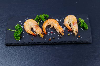 Siyah arkaplanda maydanozlu, tuzlu ve biberli büyük çiğ karidesler.