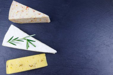 Siyah tahta zemin üzerinde çeşitli peynir türleri. Üst görünüm