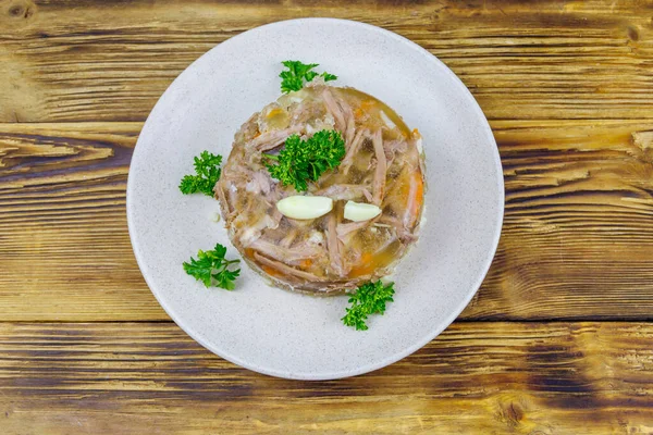 Meat aspic in a plate on a wooden table. Top view. Traditional russian dish