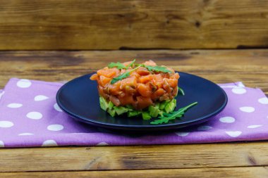 Avokado ve roka ile ahşap masada somon tartar.