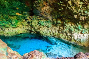 View of beautiful natural pool of crystal clear water formed in a rocky cave with stalagmites and stalagmites. Kuza cave in Zanzibar, Tanzania clipart