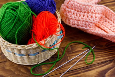 Hasır sepet, renkli örgü iplikleri, örgü iğneleri ve ahşap masa üzerine örülmüş eşarp.