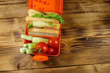Tahta bir masanın üzerinde sandviç ve taze sebzelerle beslenme çantası. Üst görünüm
