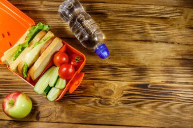 Bir şişe su, elma ve beslenme çantasıyla birlikte sandviçler ve taze sebzeler. Üst görünüm, alanı kopyala