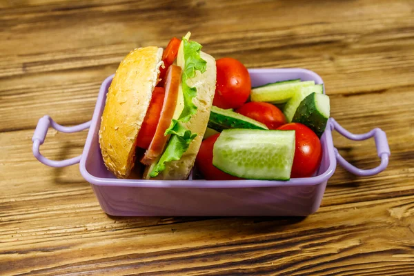 Lunch box with burgers and fresh vegetables on a wooden table