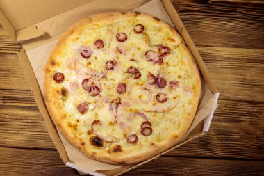 Tahta bir masanın üzerindeki karton kutuda nefis taze pizza. Üst Manzara. Yemek teslimatı, fast food, pizza teslimatı.