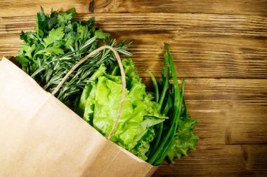 Yeşil soğanlı kağıt torbası, biberiye, marul yaprakları ve ahşap masada maydanoz. Üst Manzara. Sağlıklı gıda ve market alışverişi kavramı
