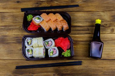 Plastik kutularda suşi ruloları, soya sosu ve ahşap masada yemek çubukları. Üst Manzara. Plastik kaplarda suşi servis etmek için suşi.