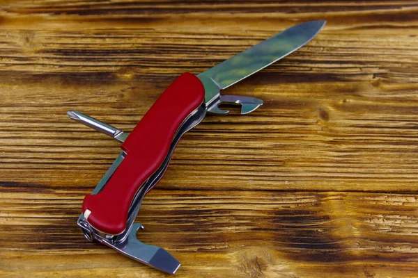 Red all purpose pocket knife on a rustic wooden background. Top view