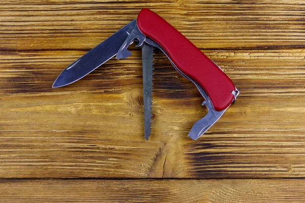 Red all purpose pocket knife on a rustic wooden background. Top view