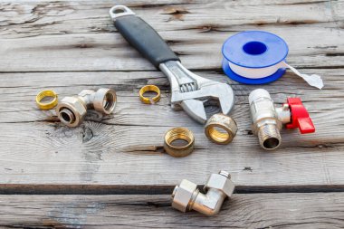 Çeşitli tesisat yedek parçaları, bant mühürleme ve ahşap arka planda ayarlanabilir ingiliz anahtarı.