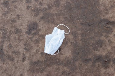 Kirli, tek kullanımlık tıbbi maske. Asfalt sokağa çöp olarak atılmış. COVID-19 sırasında israf. Koronavirüs salgınından kaynaklanan kirlilik