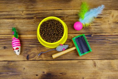 Kasede kuru kedi maması, kedi oyuncakları ve ahşap arka planda evcil hayvan fırçası. Üst Manzara. Hayvan bakımı konsepti