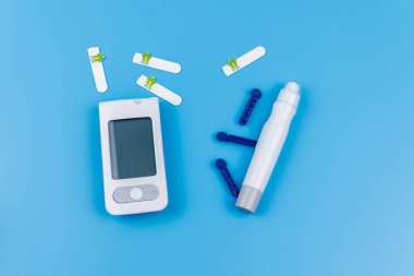 Dijital glukometre, tükenmez kalem, tek kullanımlık iğneler ve pastel mavi arka planda test şeritleri. Üst Manzara. Diyabet kavramı