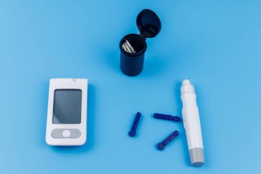 Dijital glukometre, tükenmez kalem, tek kullanımlık iğneler ve pastel mavi arka planda test şeritleri. Üst Manzara. Diyabet kavramı