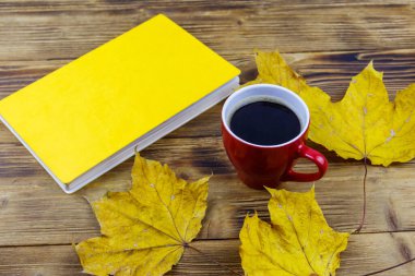 Bir fincan kahve, kitap ve sonbahar akçaağaç yaprakları ahşap masada. Sonbahar rahat konsepti