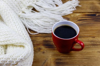 Ahşap masada örülmüş beyaz eşarp ve bir fincan kahve. Kış konsepti